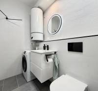 A bathroom in a one-room apartment with a washing machine, boiler, and a mirror in a circular frame.