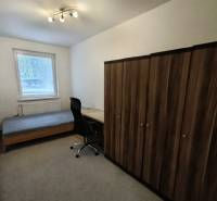 A room in a 4-room apartment with a bed, table, chair, and wardrobe on a carpet.