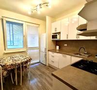 A kitchen in a 4-room apartment with a wood-patterned floor, white cabinets, and a dining area.