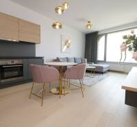 Living room with kitchen, wooden decor flooring, light-colored sofa, dining table, flowers.