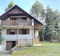 A cottage in Borský Svätý Jur surrounded by greenery and trees, with a wooden balcony.