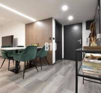 Interior of a 4-room apartment with a wooden decor floor, dining table, and green chairs.