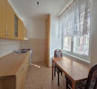 A kitchen with wooden cabinets, a table, and two chairs in a three-room apartment.