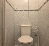 A toilet with white ceramic tiles in a 3-room apartment.