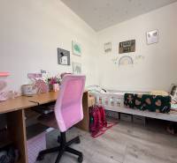 Children's room with a desk, pink chair, and a bed with decor for a child.