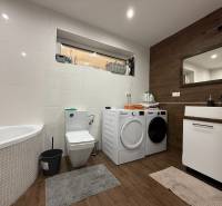 A bathroom in a family house with a bathtub, washing machine, dryer, and a floor with a wooden decor.
