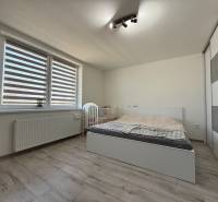 A bright bedroom in a family house with a bed, a wardrobe, and a wooden-patterned floor.