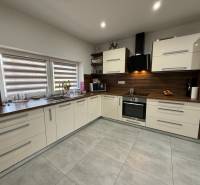 A kitchen in a family house with large windows and built-in appliances, flooring with a wooden decor.