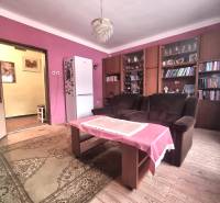 Living room of a family house with pink walls, wood-patterned flooring, and a bookshelf.