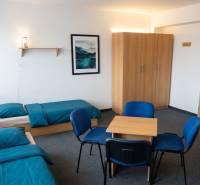 A room with two beds, blue bed linen, a wardrobe, a table, and four chairs.