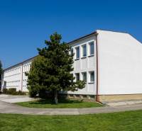 A building in Šoporňa surrounded by greenery and trees, with a clear blue sky.