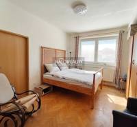 A room in a 3-room apartment with a bed, a table, a wooden decor floor, and yellow walls.
