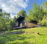 A cottage in Horná Mariková surrounded by green trees on a sunny slope under a blue sky.