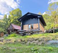 A cottage in Horná Mariková, surrounded by nature and wooden structures, on a sunny day.