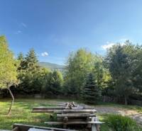 Nature in Horná Mariková with a cottage, a table with benches surrounded by trees and mountains.