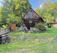 A wooden cabin in Horná Mariková surrounded by greenery and stacks of wood.