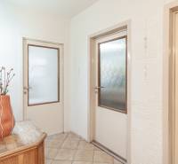 A hallway in a 3-room apartment with a flower on a wooden table and a door with glass.