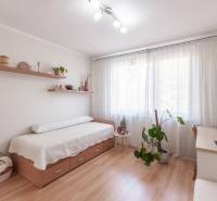 A bright room with a bed, a desk, and a wooden floor in a three-room apartment.