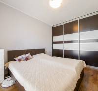 A bedroom in a three-room apartment with a wooden decor floor and a built-in wardrobe.