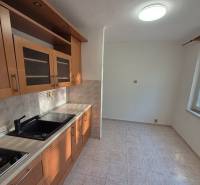 A kitchen in a studio apartment with light cabinets and ceramic tiles.