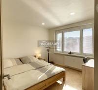 A bedroom in a studio apartment with wood-patterned flooring and large windows.