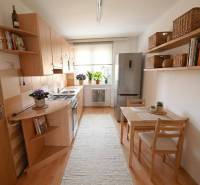 A kitchen in a 2-room apartment with a wooden decor floor, a dining table, and shelves.