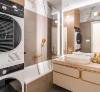 A bathroom in a 3-room apartment with a bathtub, sink, dryer, and elegant gold accessories.