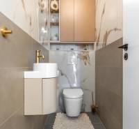 A toilet with a sink, a gold faucet, and marble-patterned tiles in a three-room apartment.