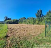 A plot for living in Hosťová with fencing and surrounding greenery under a blue sky.