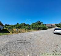 Land - housing in Hosťová: gravel road, fenced plot, parked car next to it.