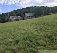 A grassy slope with buildings in the background, surrounded by nature in Horný Tisovník, ideal for residential land.
