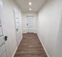 A hallway in a 3-room apartment with white doors and a wooden-patterned floor.