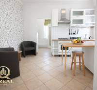 A kitchen with a bar counter, fruit, and chairs in a studio apartment.