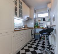 A kitchen in a 2-room apartment with black and white tiles and white cabinets.