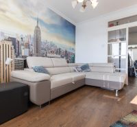 Living room in a 2-room apartment with a beige sofa, city photo wallpaper, wooden decor flooring.