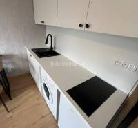 A kitchenette in a studio apartment with white cabinets and a wood-patterned floor.