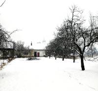 A snowy yard of a family house in Kameňany with fruit trees.