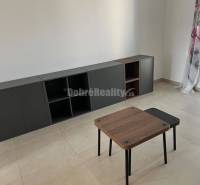 Living room in a two-room apartment with tiles, a table, and a dark cabinet.