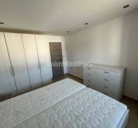 Bedroom in a 2-room apartment with white furniture and a wood-patterned floor.