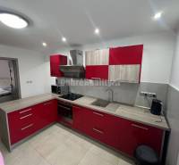 A kitchen with red cabinets and a wood-patterned floor in a two-room apartment.