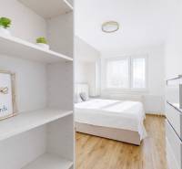 Bright bedroom in a 3-room apartment with wood-patterned flooring, shelves, and decorations.