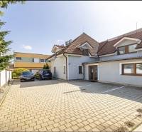 A family house in Bratislava-Vrakuňa, on Podpriehradná Street, with a paved parking lot and parked cars.