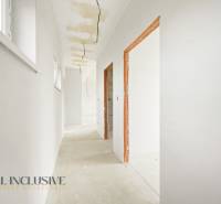 A bright hallway in a cottage with a raw floor, white walls, visible cables.