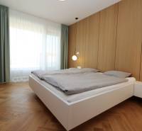 A bedroom in a 4-room apartment with wood-patterned flooring, white furniture, and a large window.