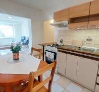 A kitchen in a 2-room apartment with a seating area, light flooring, and a dining table.