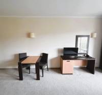 A room with a carpet contains a table, chairs, and a desk with a monitor.