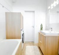 A bathroom with a bathtub, sink, and washing machine in a 3-room apartment with a wooden decor floor.
