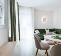 A living room with a wooden decor floor, a green sofa, and a dining table in a 3-room apartment.