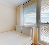 A bed in a studio apartment with a view through the blinds on the window.