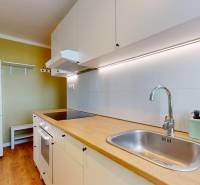 The kitchen in a studio apartment with white cabinets and a wood-patterned floor.